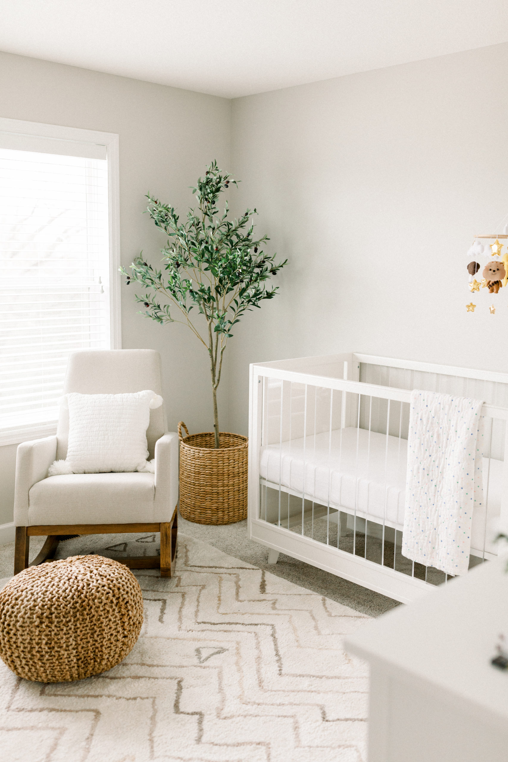 neutral elegant baby nursery with white crib and olive tree